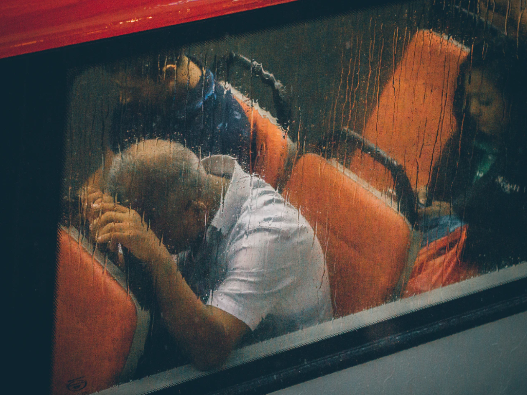 A rainy day on a bus with a man with his head in his hands.